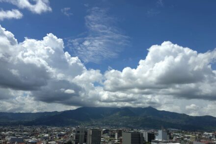 San José Skyline Beneath Mountain Clouds, Panoramic view of San José, Costa Rica, with the city skyline, surrounding mountains, and dramatic cloud formations rising above the Central Valley